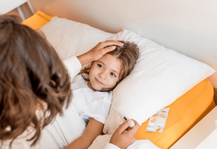 Child in bed with a care giver taking their temperature