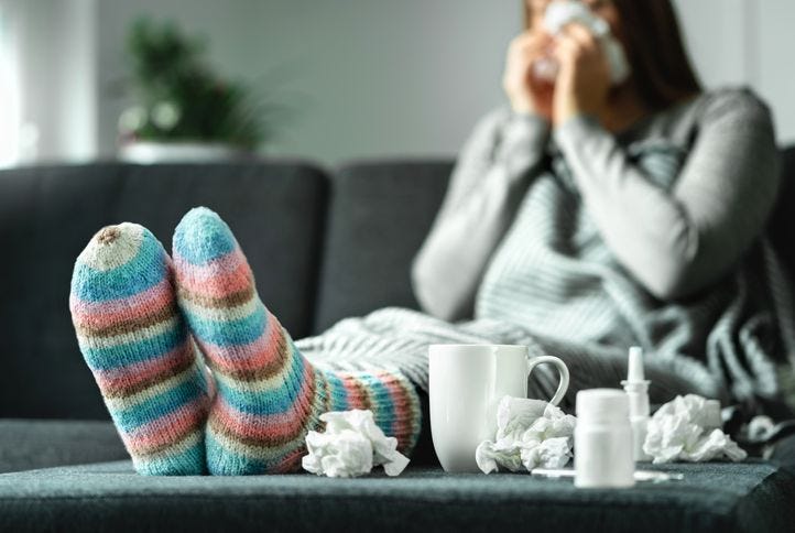 Person sitting on a couch with a box of tissues and medicines